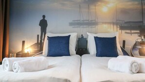 Habitació d'hotel amb llit, almoines, una tauleta de nit i vista al capvespre sobre un port esportiu.