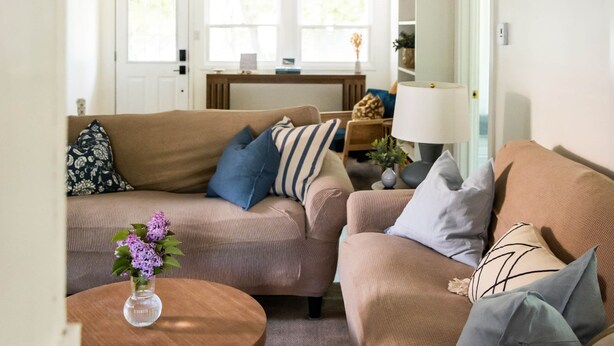 En hyggelig stue med en brun sofa, et rundt træbord og en vase med blomster.