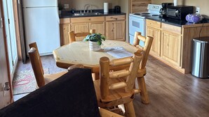 Una cocina con armarios de madera, una mesa de comedor con sillas, un refrigerador, un microondas y un letrero en la pared.