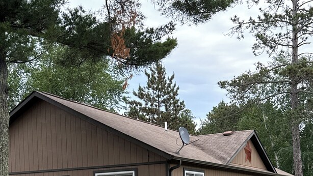 Una cabaña de dos pisos con un brasero en el jardín, mobiliario exterior y una antena parabólica.