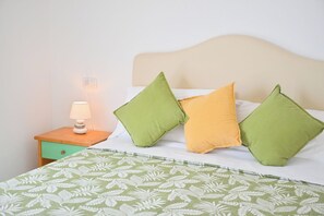 Ein Bett mit einem gemusterten Überwurf, ein Nachttisch mit einer Lampe und Kissen in Grün und Gelb.