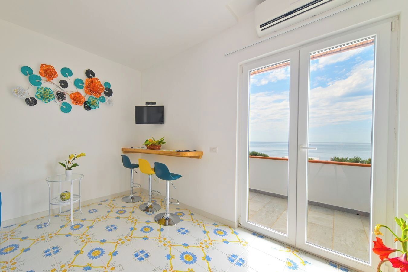 A room with a balcony, a TV mounted on the wall, and a table with chairs.