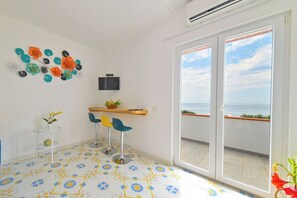 Ein Zimmer mit Balkon, einem an der Wand befestigten Fernseher und einem Tisch mit Stühlen.
