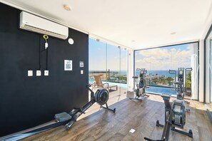 Une salle de sport moderne équipée de matériel d’exercice, une grande fenêtre donnant sur la mer et un mur noir orné d’un code QR.