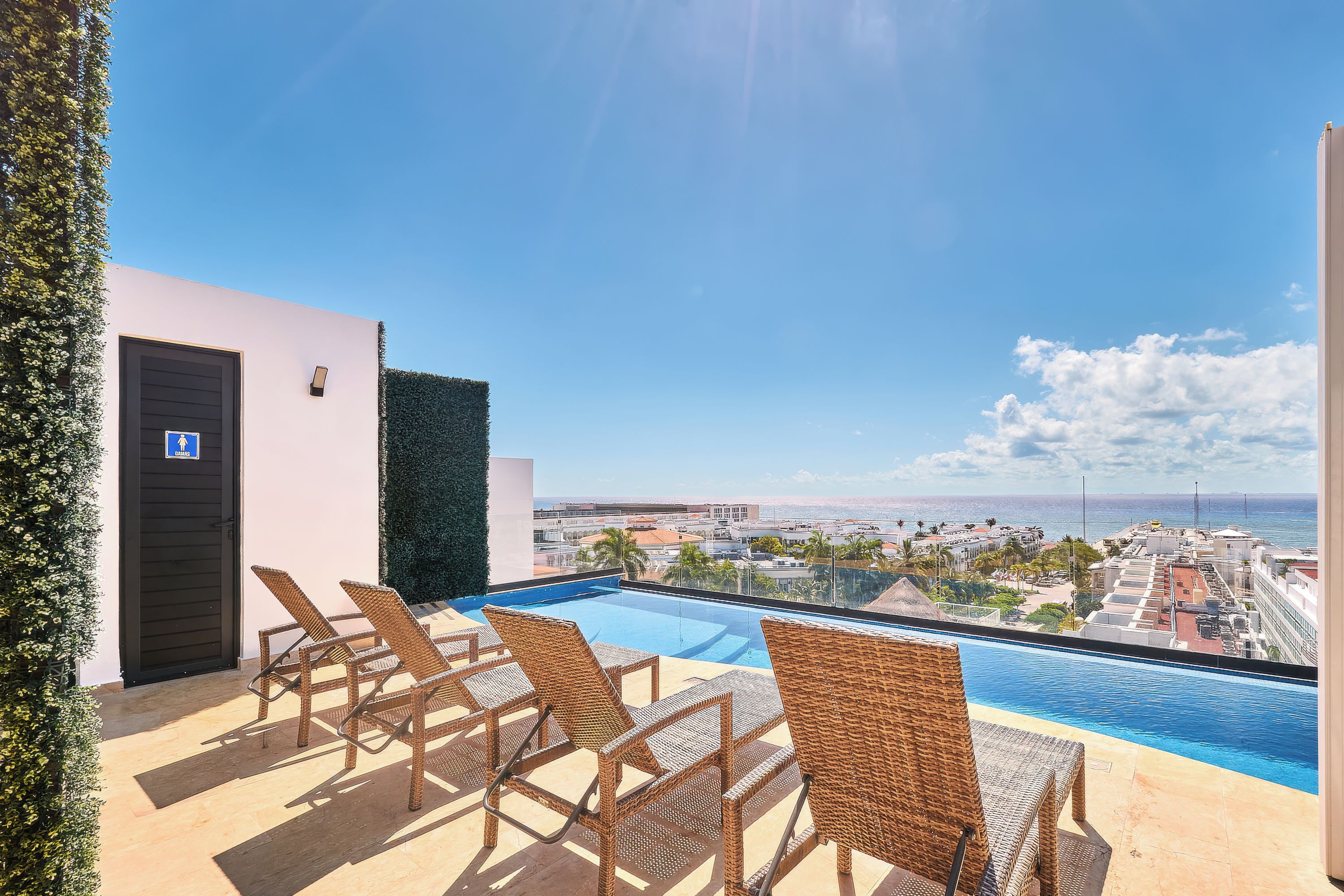 A rooftop pool area with lounge chairs and a view of the city and ocean.