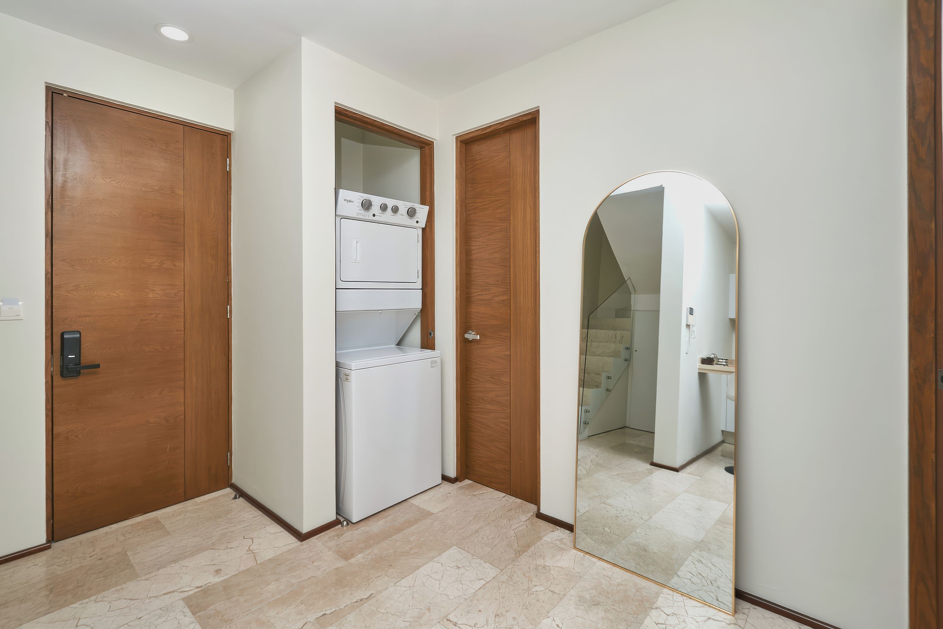 Un pasillo con un refrigerador blanco, puertas de madera y un espejo que refleja un baño.