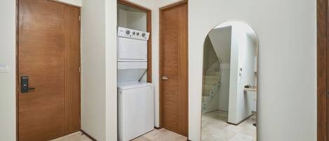 Un pasillo con un refrigerador blanco, puertas de madera y un espejo que refleja un baño.