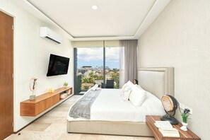 Habitación de hotel moderna con una cama grande, un televisor de pantalla plana, una mesa consola de madera y vistas de la ciudad a través de un ventanal amplio.