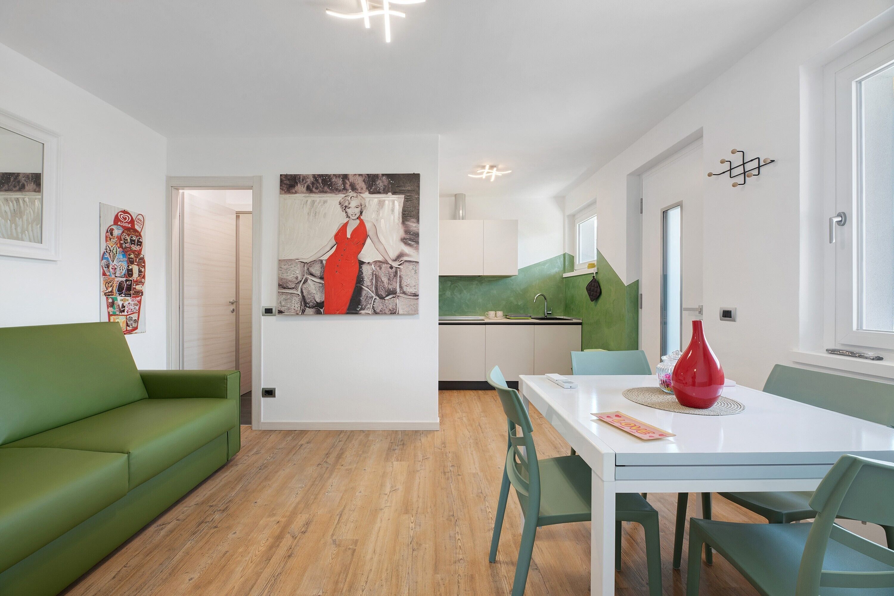 Ein modernes Wohnzimmer mit einem grünen Sofa, einem Esstisch mit Stühlen und einer Küche im Hintergrund.
