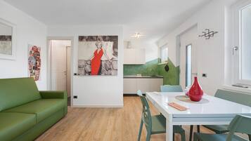 Ein modernes Wohnzimmer mit einem grünen Sofa, einem Esstisch mit Stühlen und einer Küche im Hintergrund.
