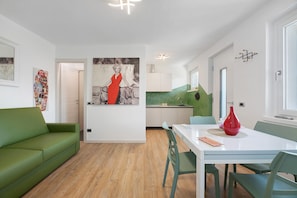 A modern living room with a green sofa, a dining table with chairs, and a kitchen in the background. - Apartment 'Casa Ada' with Lake View, Balcony and Wi-Fi (Colico)