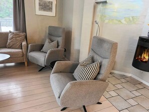 A living room with two grey armchairs, a white coffee table, and a fireplace with a visible fire. - 9 Person Holiday Home in Saeby (Sæby)