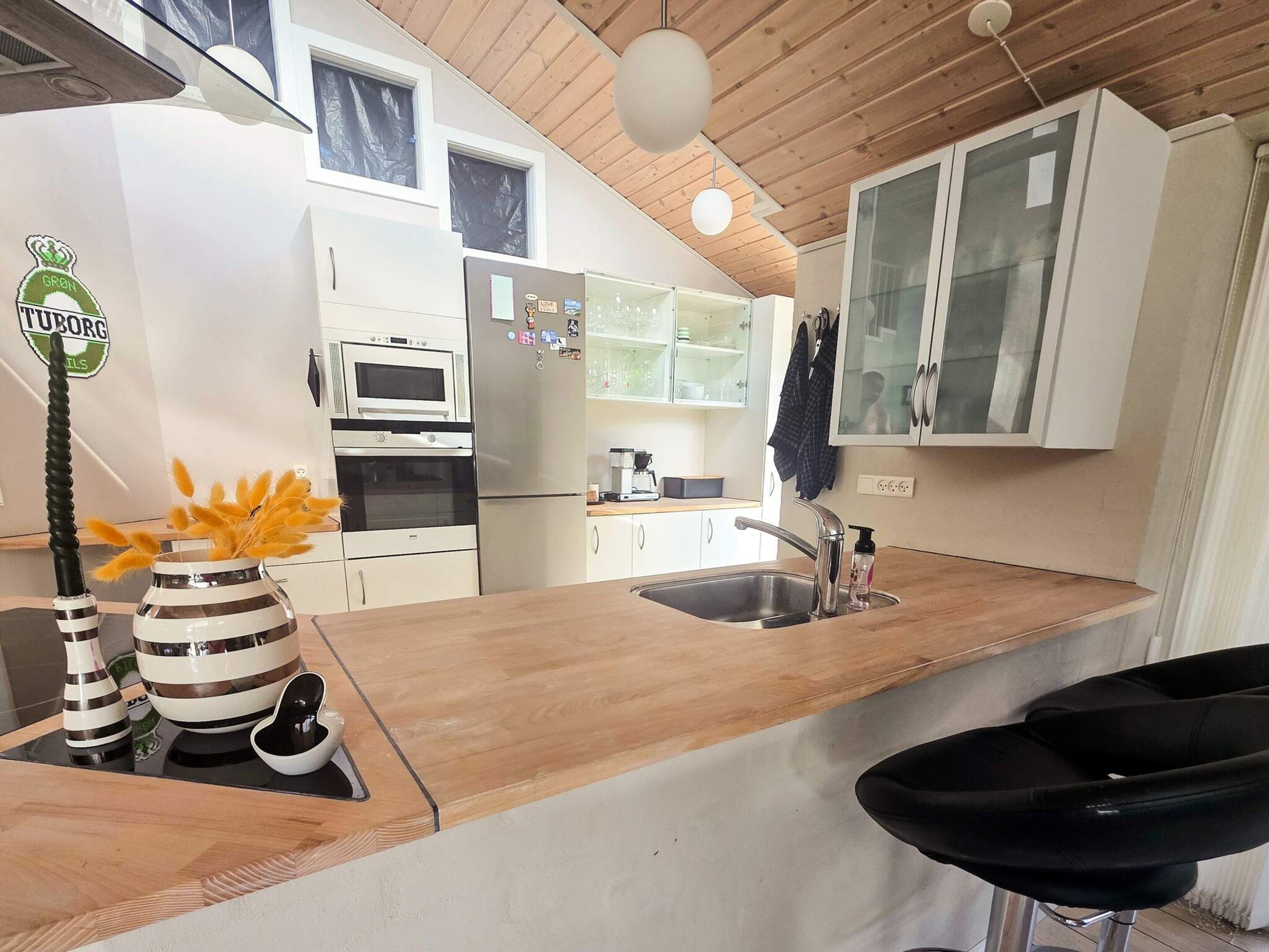 A modern kitchen with white cabinets, a stainless steel refrigerator, a microwave, and a wooden countertop.
