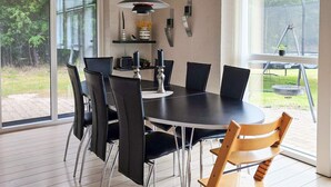 A modern dining area with a round table, black chairs, and a hanging pendant light. - 9 Person Holiday Home in Saeby (Sæby)