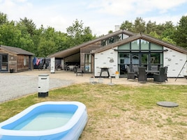 Una casa moderna con un porche techado, mobiliario de exterior y piscina.
