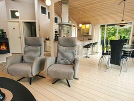 Una sala de estar moderna con dos sillones grises, una chimenea y una zona de comedor con mesa y sillas.