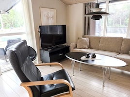 Una sala de estar con un sillón de cuero negro, un mueble de entretenimiento negro con un televisor, un sofá color beige y una mesa de centro redonda.
