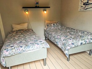 Two single beds with floral bedding, a wall-mounted shelf with a small figurine, and a painting on the wall. - 9 Person Holiday Home in Saeby (Sæby)