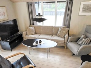 A living room with a sofa, armchair, TV, coffee table, and a pendant light. - 9 Person Holiday Home in Saeby (Sæby)