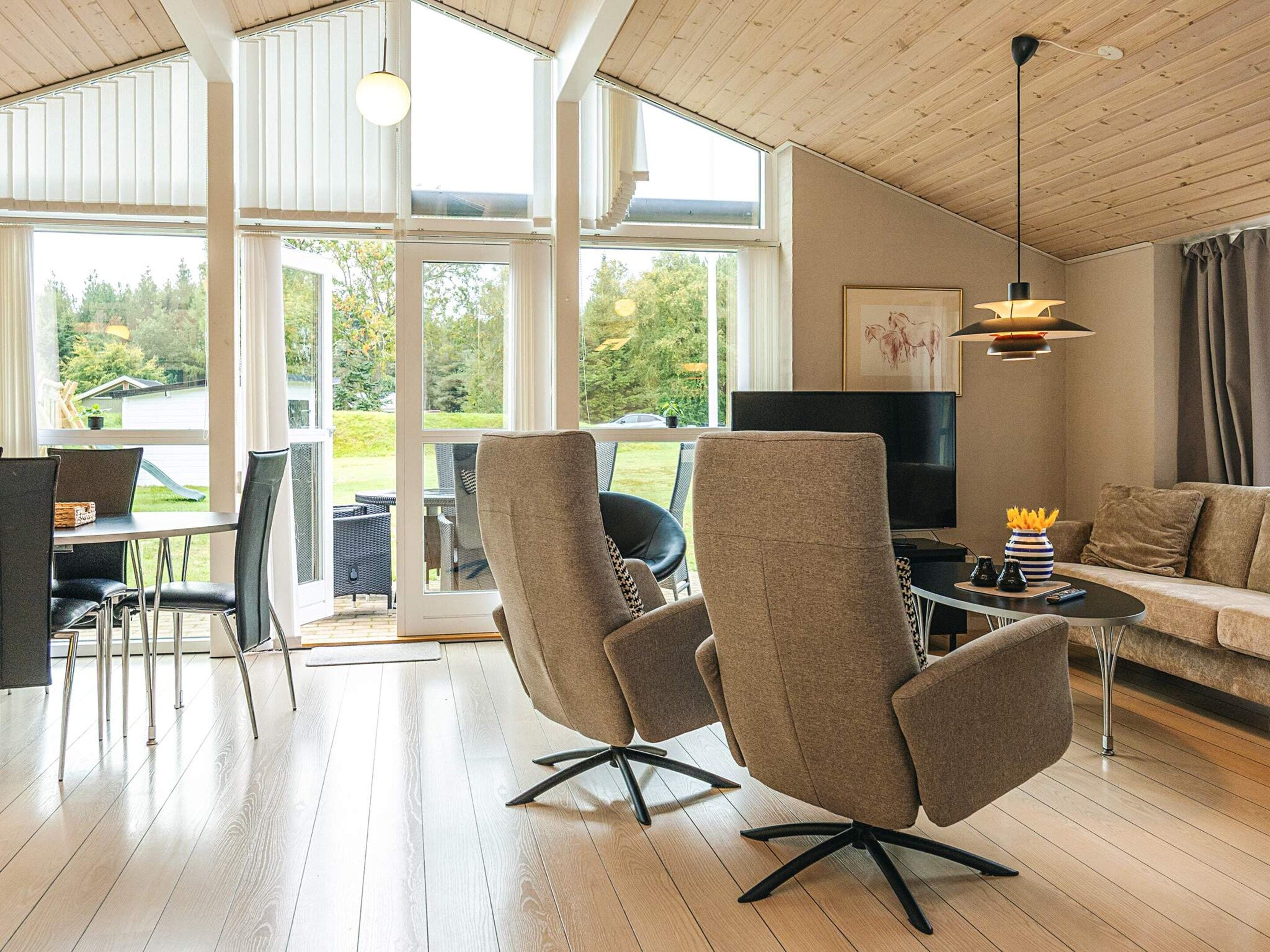 A modern living room with a large window, a sofa, a TV, and a dining area.