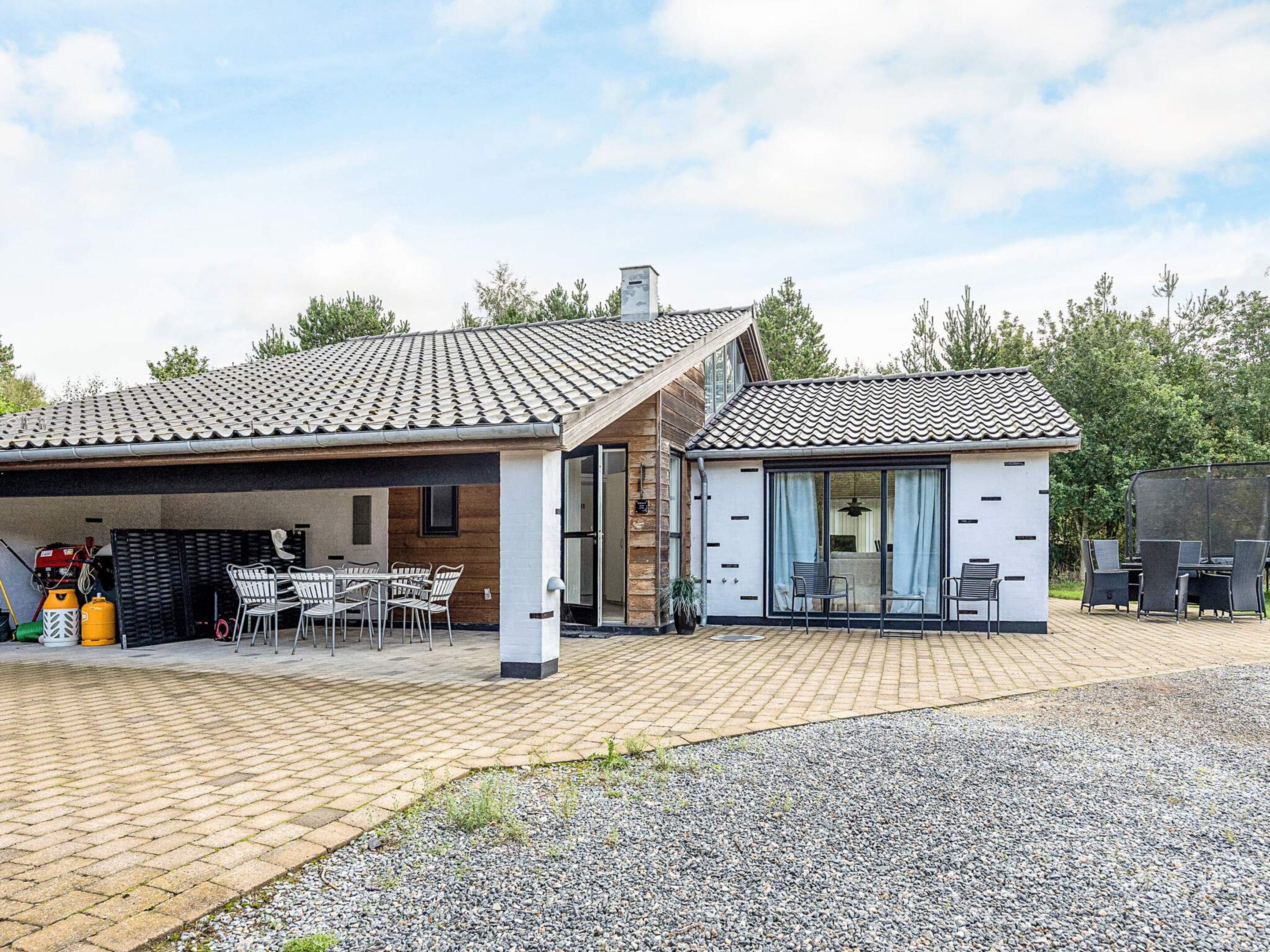Een tweelaags huis met een overdekte patio, buiten zitplaatsen en een garage met een voertuig.
