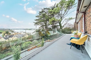 Ein Balkon mit Glasgeländer, einem gelben Stuhl und einem Tisch mit Blumenvase.