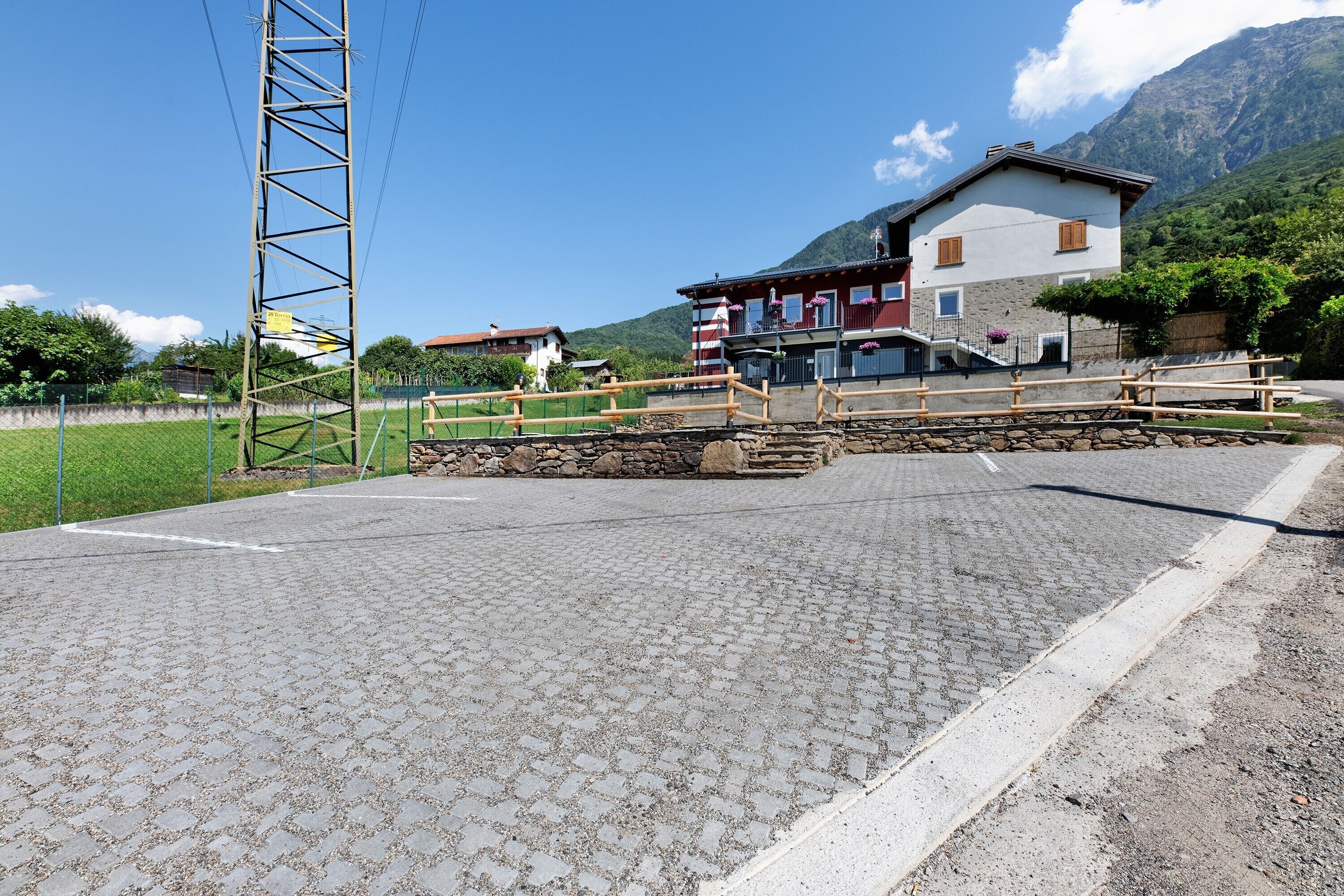 Una zona pavimentada amb un pont de fusta, una paret de pedra i un edifici amb les muntanyes de fons.