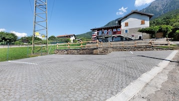 Una zona pavimentada amb un pont de fusta, una paret de pedra i un edifici amb les muntanyes de fons.