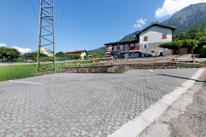 A paved area with a wooden bridge, a stone wall, and a building with a mountain backdrop.