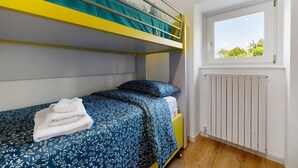 A bunk bed with a blue and white patterned bedspread, a white towel, and a window with a view of greenery. - Apartment 'Casa Mike' with Lake View, Private Garden and Wi-Fi (Colico)