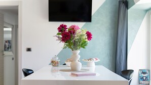 A modern dining area with a white table, a vase of flowers, a small jar of candies, and a cake on a white stand. - Apartment 'Casa Mike' with Lake View, Private Garden and Wi-Fi (Colico)