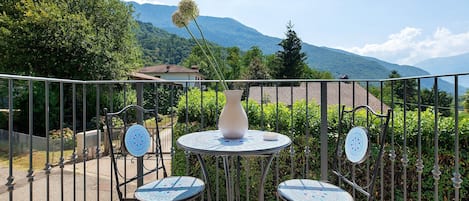 A balcony with a table and chairs, a vase, and a view of mountains.