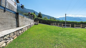 Un mur de pedra amb una barana metàl·lica, un prat i una tanca de fusta.