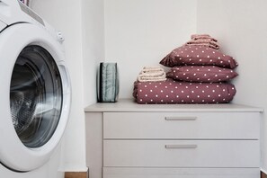 A washing machine, a stack of folded towels, and a drawer unit in a room.