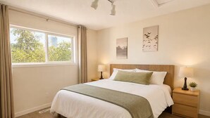 Une chambre à coucher avec un grand lit, deux tables de chevet, une fenêtre avec des rideaux et des œuvres d’art accrochées au mur.