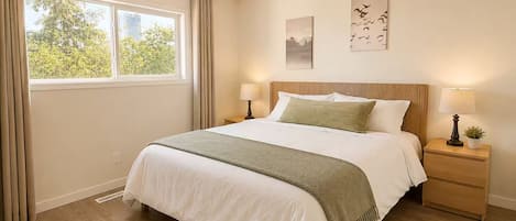 Un dormitorio con una cama grande, dos mesitas de noche, un ventanal con cortinas y una obra de arte en la pared.