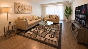 Un salon avec un canapé, une table basse, un téléviseur et un tableau accroché au mur.