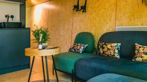 Un accogliente soggiorno con soffitto in legno, un divano verde con cuscini floreali, un piccolo tavolino con una pianta e un mobiletto nero.