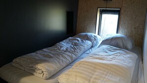 Un letto singolo con biancheria da letto bianca in una stanza con una finestra e un punto luce a parete.