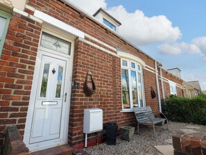 A brick house with a white door, a window with a white frame, and a small garden area with gravel and a bench. - 8 Percy Terrace (Sunderland)