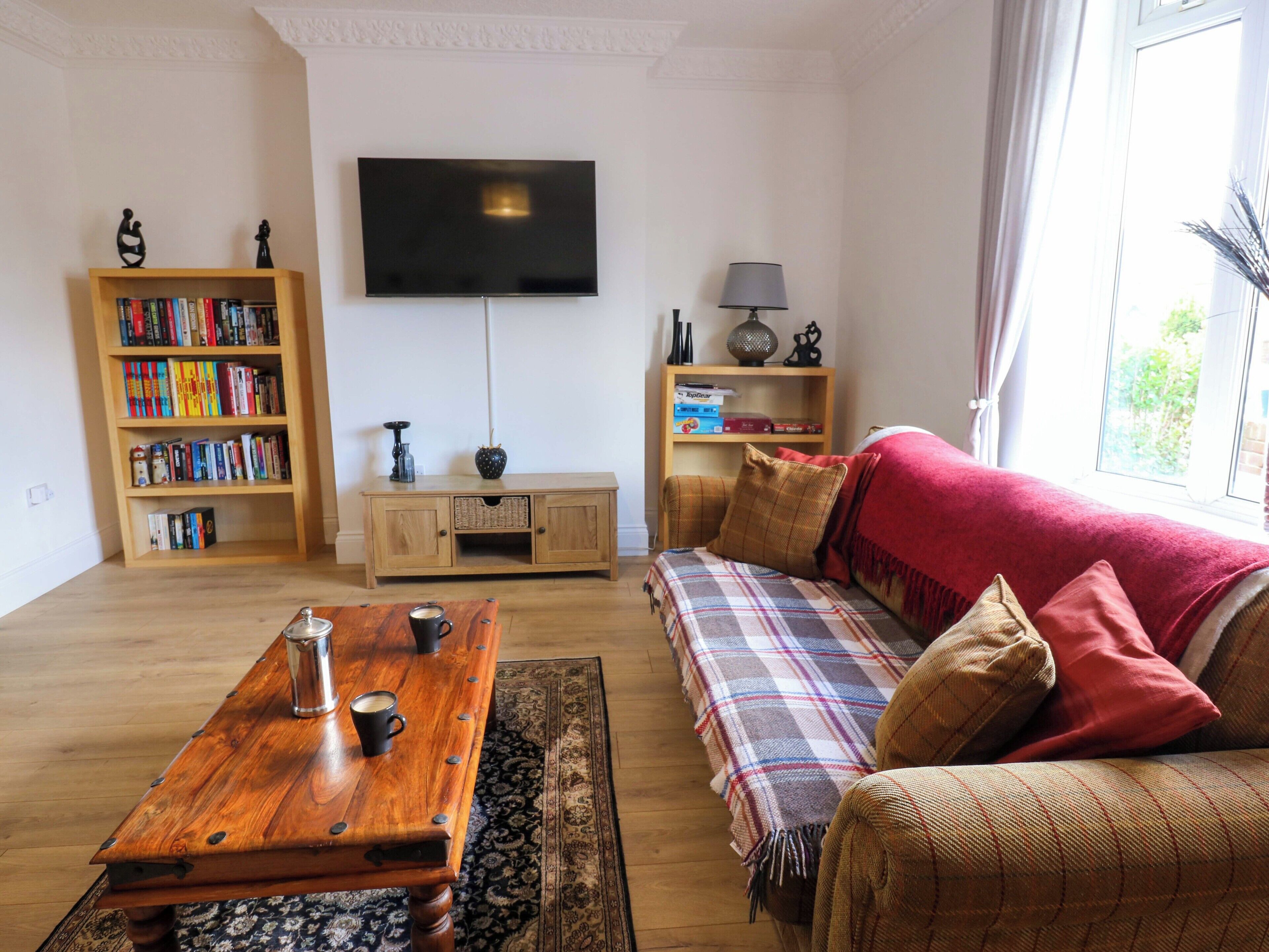 A living room with a wooden coffee table, a sofa, a television, a bookshelf, and a window.