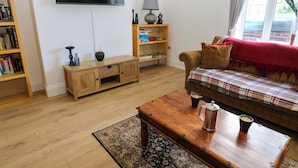 A living room with a flat-screen TV, a wooden coffee table with a cup and a thermos, a sofa with a plaid blanket, a bookshelf, and a lamp on a side table. - 8 Percy Terrace (Sunderland)