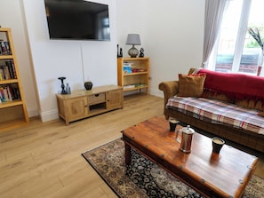 A living room with a flat-screen TV, a wooden coffee table with a cup and a thermos, a sofa with a plaid blanket, a bookshelf, and a lamp on a side table. - 8 Percy Terrace (Sunderland)