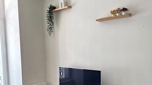 A modern living room with a flat-screen TV on a wooden stand, a radiator, a small round table, and two wall-mounted shelves with plants. - Apartment in the heart of Annonay (Annonay)