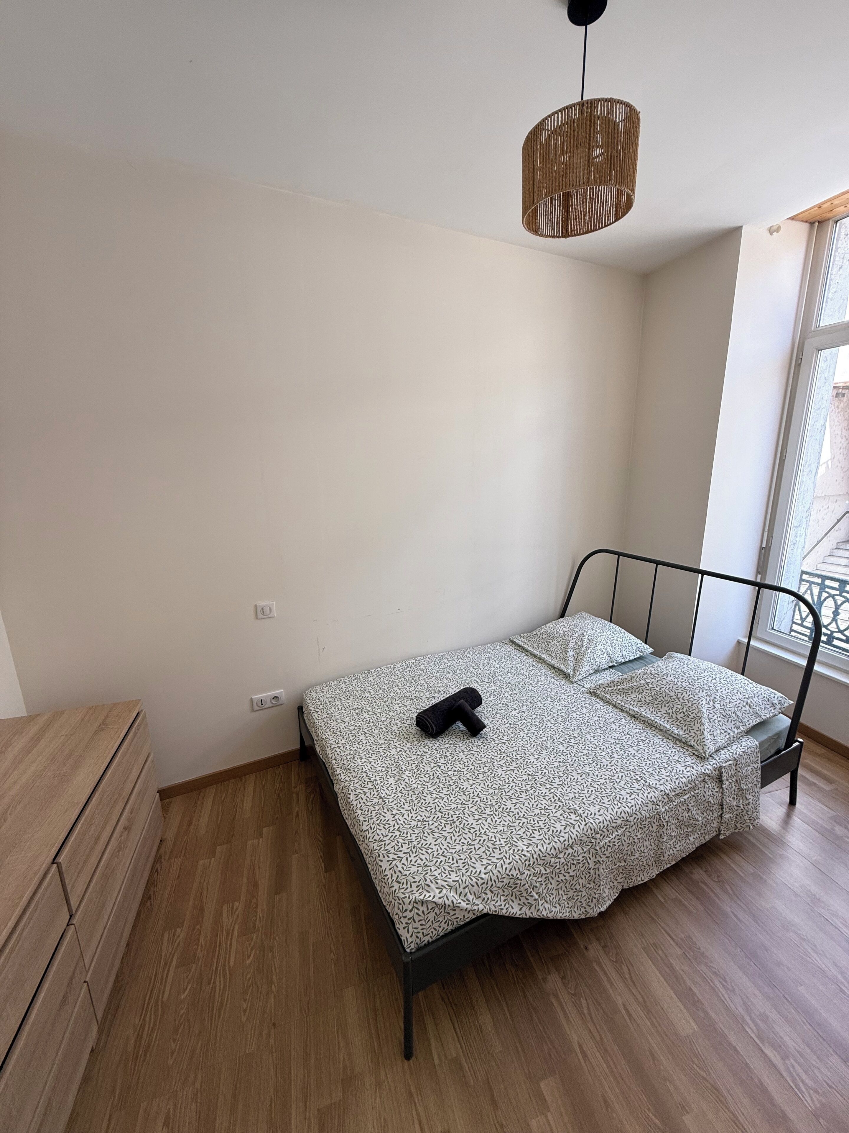 Un dormitorio con cama, cómoda de madera, lámpara colgante y ventana con vistas.