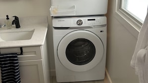 A compact washer and dryer unit with a white countertop and sink, a mirror, and a window with a view. - Cozy, newly renovated home with a gorgeous fireplace and office space. (Midland)