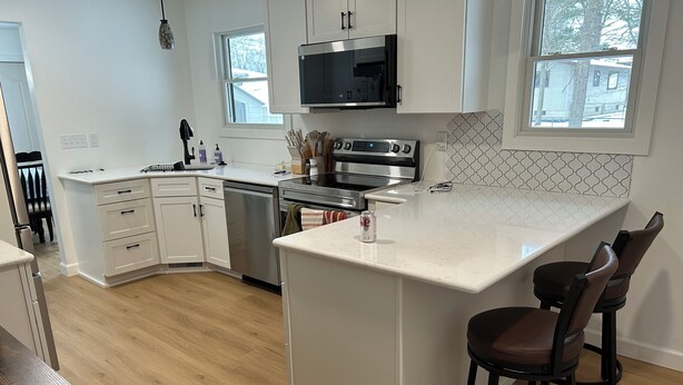 A modern kitchen with white cabinetry, a stainless steel stove, a microwave, and a large island with bar stools. - Cozy, newly renovated home with a gorgeous fireplace and office space. (Midland)