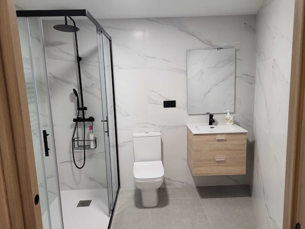 A modern bathroom with a glass-enclosed shower, a toilet, a vanity with a mirror, and marble tiles.