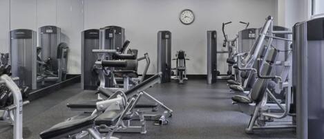 A gym with various exercise machines, a clock on the wall, and a mirror.