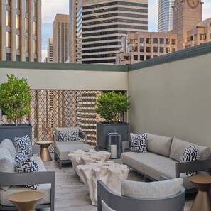 Eine Dachterrasse mit moderner Sitzgelegenheit, zwei Blumentöpfen und Blick auf Stadtgebäude.